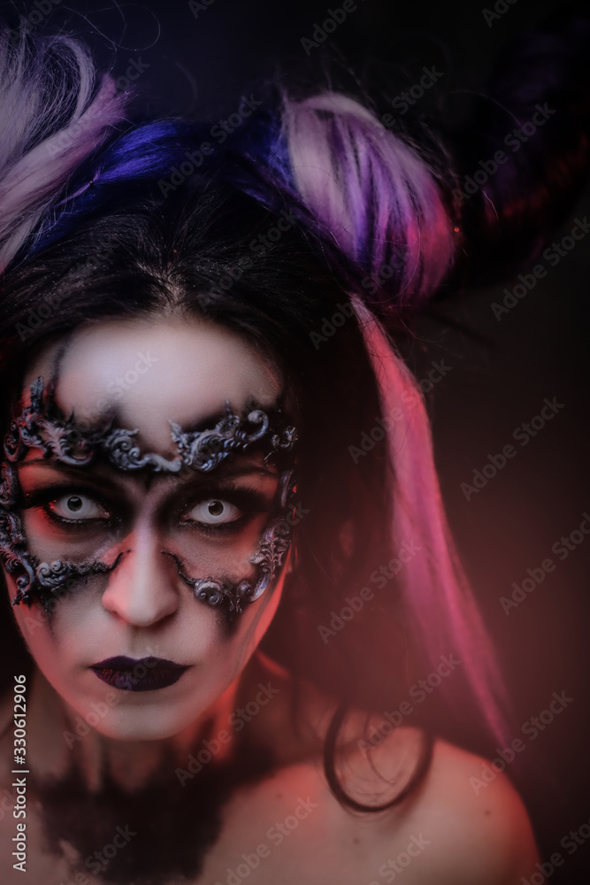 Fototapeta premium Close up vertical photo of a mystic young girl in a magic creature cosplay, wearing dark banshee make-up and violet horns, looking spooky straight to camera