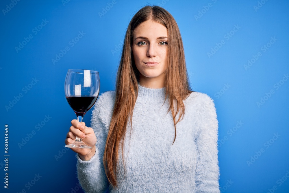 Young beautiful redhead woman drinking glass of red wine over isolated blue background with a confident expression on smart face thinking serious Young beautiful redhead woman drinking glass of red wine over isolated blue background with a confident expression on smart face thinking serious