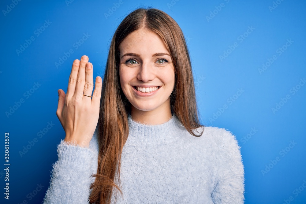 Young beautiful redhead woman wearing wedding ring on finger over blue background with a happy face standing and smiling with a confident smile showing teeth Young beautiful redhead woman wearing wedding ring on finger over blue background with a happy face standing and smiling with a confident smile showing teeth