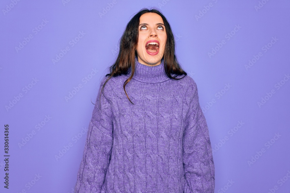 Young beautiful woman wearing casual turtleneck sweater standing over purple background angry and mad screaming frustrated and furious, shouting with anger. Rage and aggressive concept. Young beautiful woman wearing casual turtleneck sweater standing over purple background angry and mad screaming frustrated and furious, shouting with anger. Rage and aggressive concept.