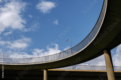 Low angle view under curvature 
concrete structural deck with steel balustrade of sidewalk for pedestrian and bicycle lanes of the bridge against blue sky. 