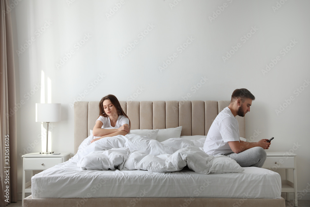 Young man preferring smartphone over his girlfriend on bed at home. Relationship problems