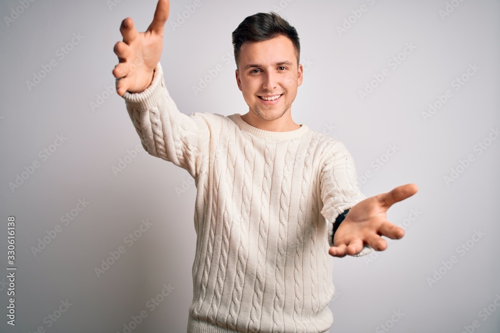 Fototapeta premium Young handsome caucasian man wearing casual winter sweater over white isolated background looking at the camera smiling with open arms for hug. Cheerful expression embracing happiness.