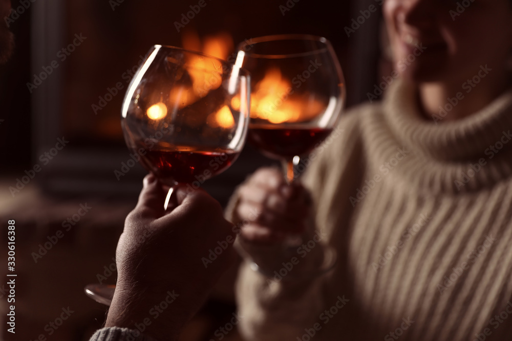Lovely couple with glasses of wine near fireplace at home, closeup. Winter vacation Lovely couple with glasses of wine near fireplace at home, closeup. Winter vacation