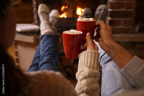 Couple with cups of delicious cocoa resting near fireplace at home, closeup. Winter vacation photo