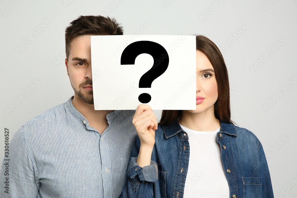 Couple holding question mark sign on light background Couple holding question mark sign on light background