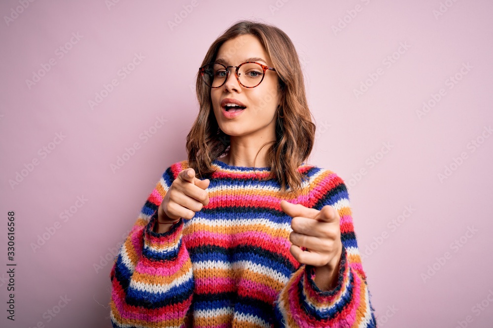 Young beautiful blonde girl wearing glasses and casual sweater over pink isolated background pointing fingers to camera with happy and funny face. Good energy and vibes. Young beautiful blonde girl wearing glasses and casual sweater over pink isolated background pointing fingers to camera with happy and funny face. Good energy and vibes.