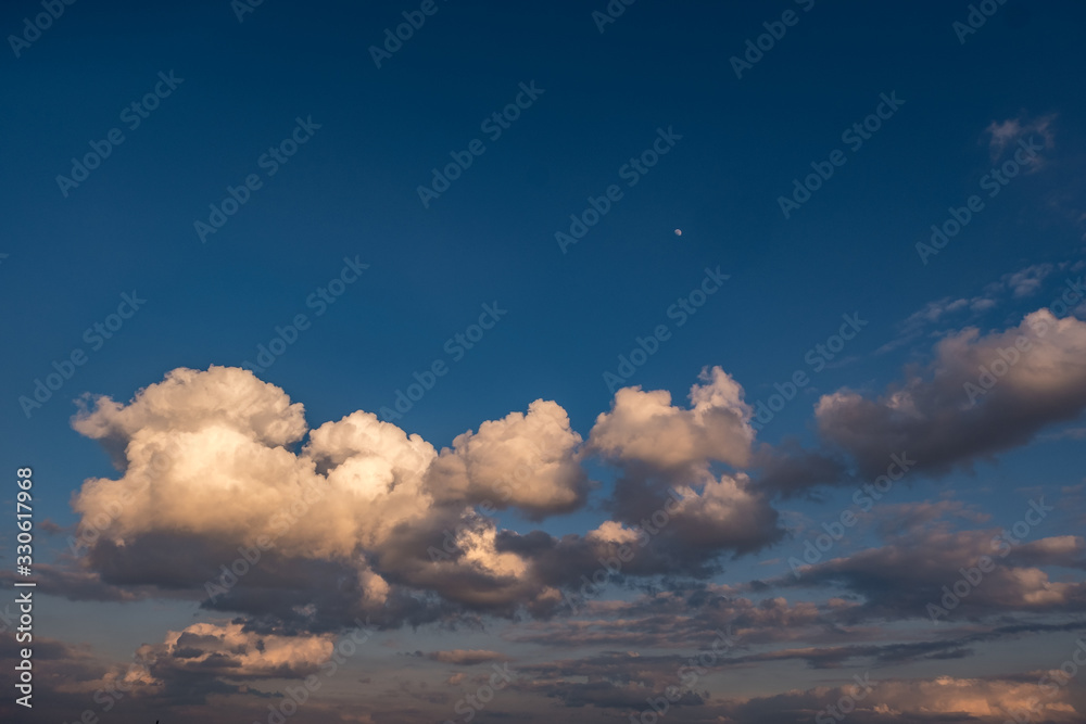 Blue sky background with evening fluffy curly rolling clouds. Good windy weather