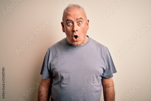 Middle age handsome hoary man wearing t-shirt standing over isolated white background afraid and shocked with surprise expression, fear and excited face.
