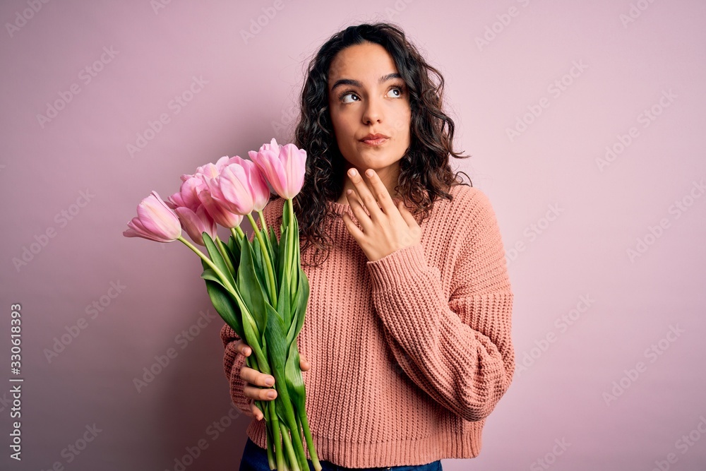 Young beautiful romantic woman with curly hair holding bouquet of pink tulips Thinking concentrated about doubt with finger on chin and looking up wondering Young beautiful romantic woman with curly hair holding bouquet of pink tulips Thinking concentrated about doubt with finger on chin and looking up wondering