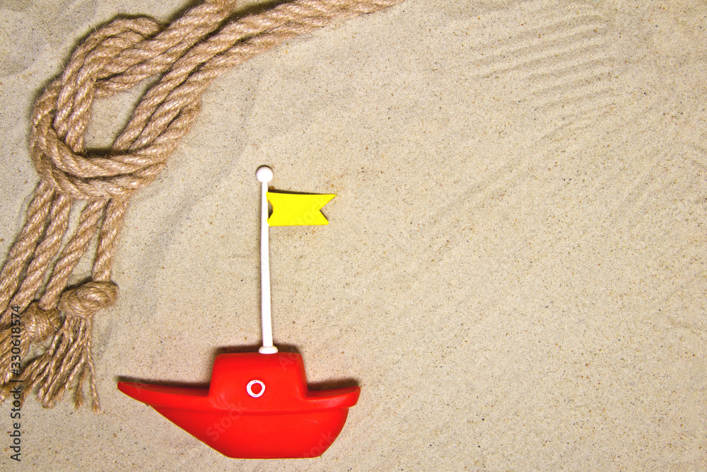 Seashells and nautical rope decoration on sand background with red toy ship Seashells and nautical rope decoration on sand background with red toy ship