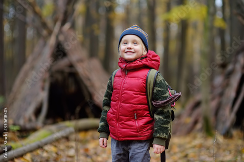 Little boy scout during hiking in autumn forest. Teepee hut on background.