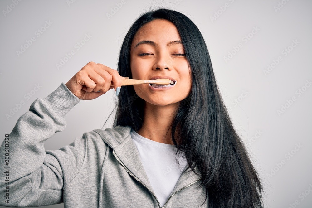 Young beautiful woman smiling happy. Standing with smile on face whasing tooth using toothbrush over isolated white background Young beautiful woman smiling happy. Standing with smile on face whasing tooth using toothbrush over isolated white background