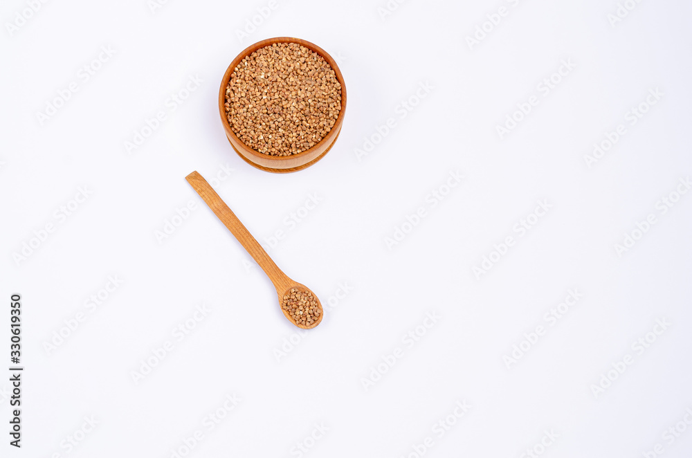 Traditional Ukrainian dry unroasted buckwheat groats in a wooden spoon and bowl on a white background copy space. Healthy foods high in protein and carbohydrates. View from above.
