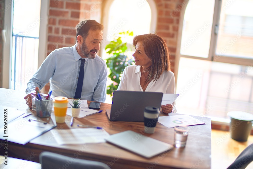 Two middle age business workers smiling happy and confident. Working together with smile on face using laptop at the office Two middle age business workers smiling happy and confident. Working together with smile on face using laptop at the office