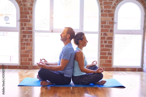 Middle age beautiful sporty couple sitting on mat practicing yoga doing lotus pose at gym photo