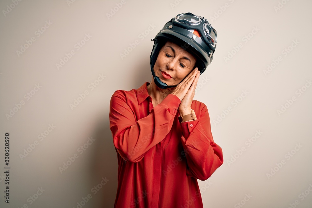 Middle age motorcyclist woman wearing motorcycle helmet over isolated white background sleeping tired dreaming and posing with hands together while smiling with closed eyes. Middle age motorcyclist woman wearing motorcycle helmet over isolated white background sleeping tired dreaming and posing with hands together while smiling with closed eyes.