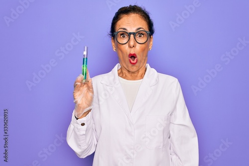Middle age senior scientist woman wearing laboratory coat holding research test tube scared in shock with a surprise face  afraid and excited with fear expression