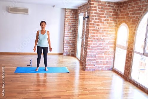 Middle age beautiful sportwoman standing on mat. Practicing yoga doing mountain pose at gym photo