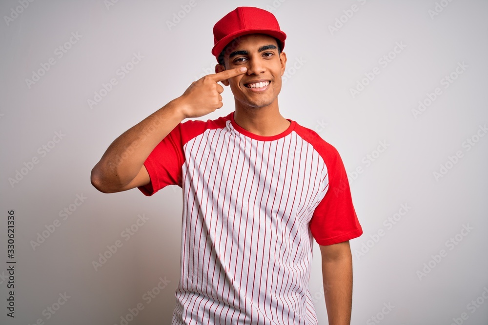 Young handsome african american sportsman wearing striped baseball t-shirt and cap Pointing with hand finger to face and nose, smiling cheerful. Beauty concept Young handsome african american sportsman wearing striped baseball t-shirt and cap Pointing with hand finger to face and nose, smiling cheerful. Beauty concept