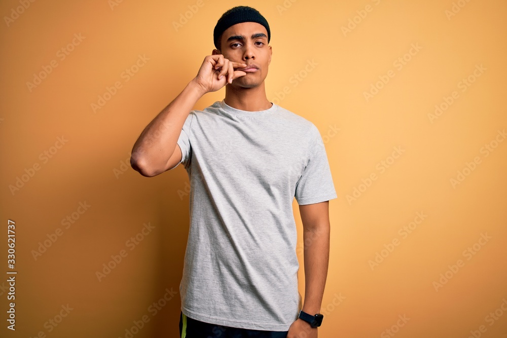 Fototapeta premium Handsome african american sportsman doing sport wearing sportswear over yellow background mouth and lips shut as zip with fingers. Secret and silent, taboo talking