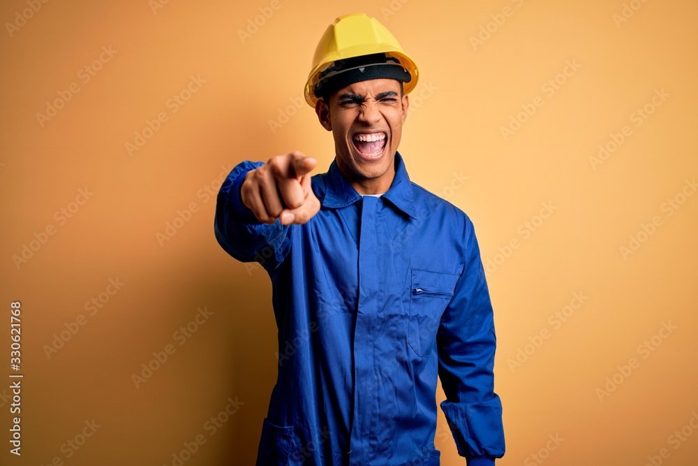Young handsome african american worker man wearing blue uniform and security helmet pointing displeased and frustrated to the camera, angry and furious with you