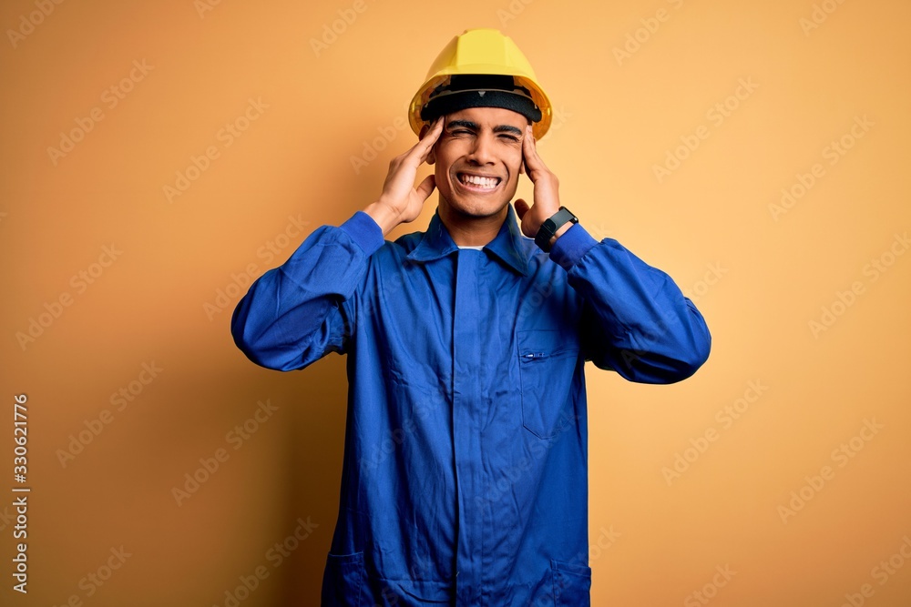 Young handsome african american worker man wearing blue uniform and security helmet covering ears with fingers with annoyed expression for the noise of loud music. Deaf concept. Young handsome african american worker man wearing blue uniform and security helmet covering ears with fingers with annoyed expression for the noise of loud music. Deaf concept.