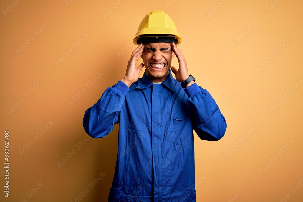 Young handsome african american worker man wearing blue uniform and security helmet with hand on headache because stress. Suffering migraine.