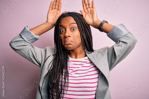 Young african american business woman standing over pink isolated background Doing bunny ears gesture with hands palms looking cynical and skeptical. Easter rabbit concept. photo