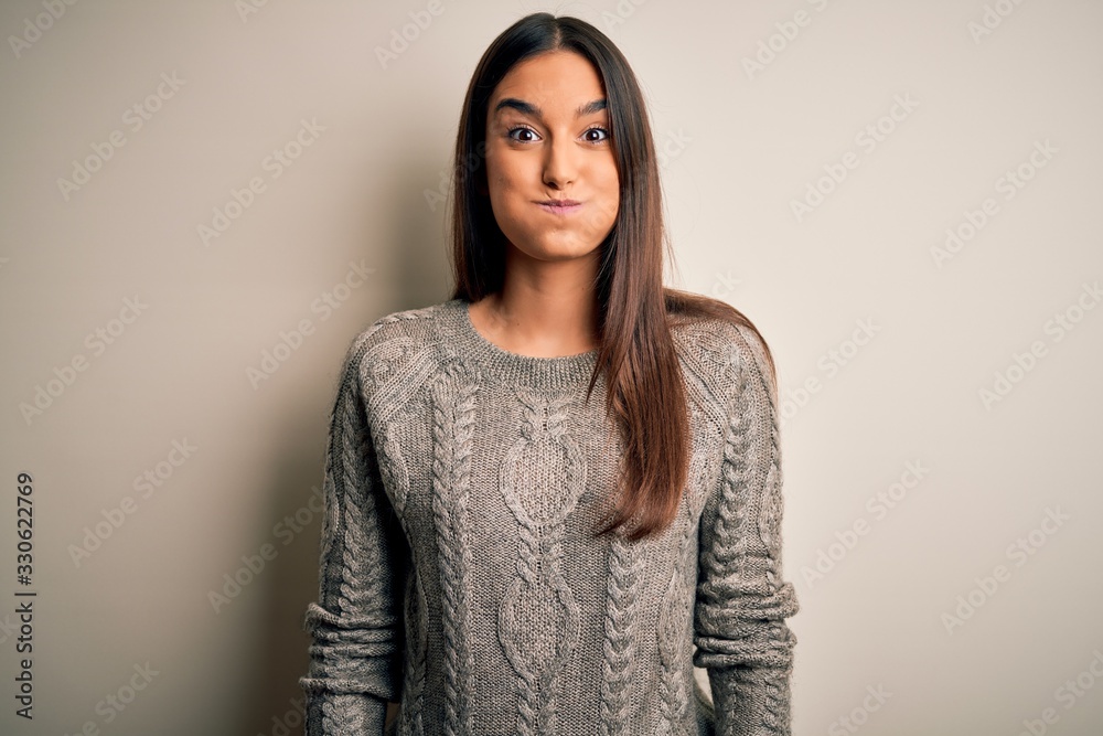 Young beautiful brunette woman wearing casual sweater over isolated white background puffing cheeks with funny face. Mouth inflated with air, crazy expression. Young beautiful brunette woman wearing casual sweater over isolated white background puffing cheeks with funny face. Mouth inflated with air, crazy expression.