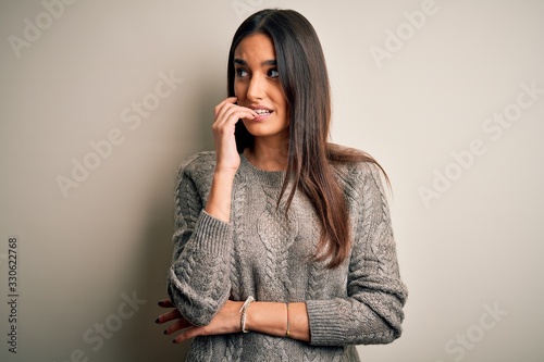 Young beautiful brunette woman wearing casual sweater over isolated white background looking stressed and nervous with hands on mouth biting nails. Anxiety problem.