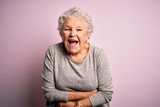 Senior beautiful woman wearing casual t-shirt standing over isolated pink background smiling and laughing hard out loud because funny crazy joke with hands on body.