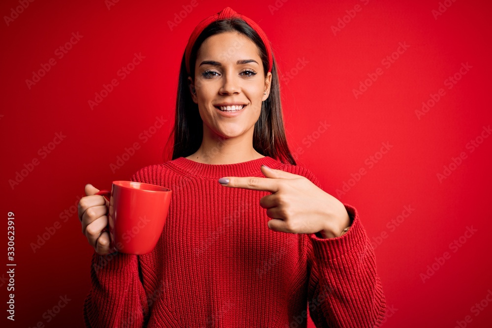 Young beautiful brunette woman drinking mug of coffe over isolated red background very happy pointing with hand and finger Young beautiful brunette woman drinking mug of coffe over isolated red background very happy pointing with hand and finger