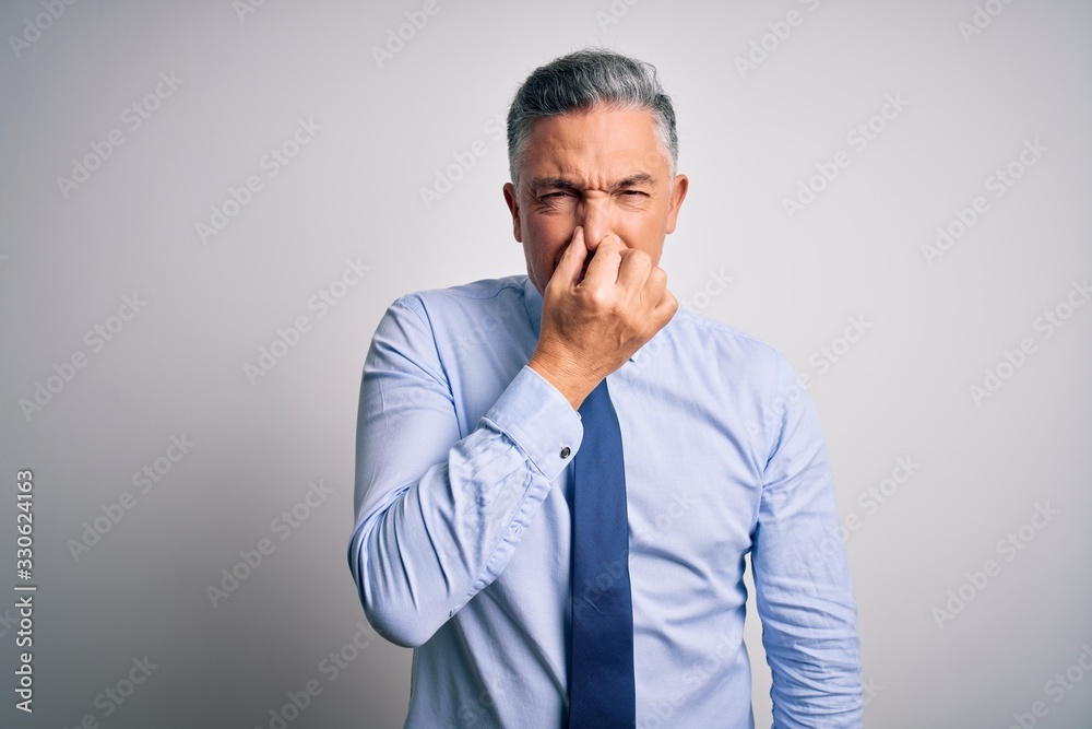 Middle age handsome grey-haired business man wearing elegant shirt and tie smelling something stinky and disgusting, intolerable smell, holding breath with fingers on nose. Bad smell Middle age handsome grey-haired business man wearing elegant shirt and tie smelling something stinky and disgusting, intolerable smell, holding breath with fingers on nose. Bad smell