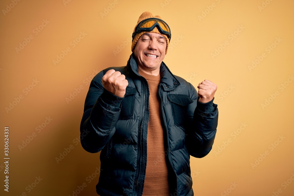 Fototapeta premium Middle age handsome grey-haired skier man on vacation wearing ski goggles excited for success with arms raised and eyes closed celebrating victory smiling. Winner concept.