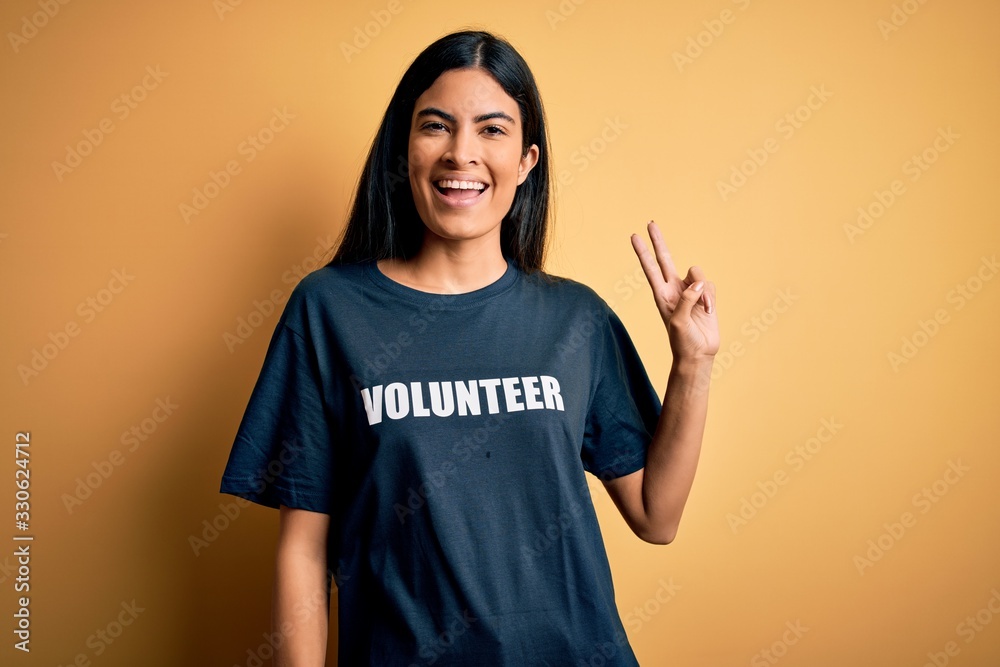 Young beautiful hispanic woman wearing volunteer t-shirt as social charity moral smiling looking to the camera showing fingers doing victory sign. Number two.