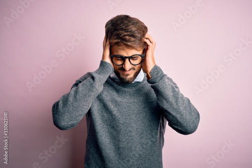 Fotografie Young handsome man with beard wearing glasses and sweater standing over pink background suffering from headache desperate and stressed because pain and migraine