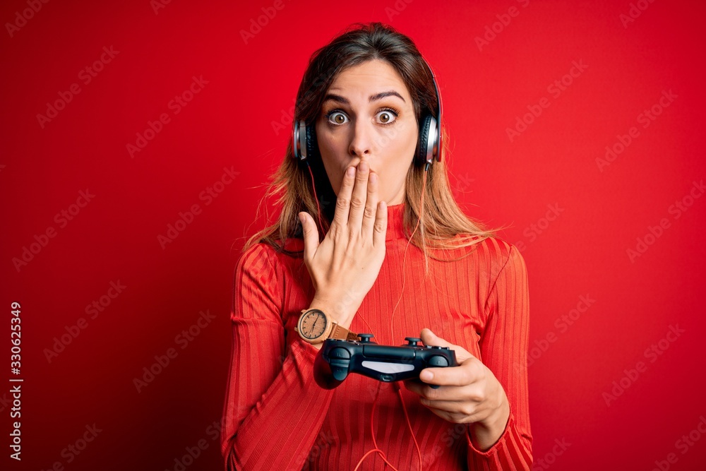 Young beautiful brunette gamer woman playing video game using joystic and headphones cover mouth with hand shocked with shame for mistake, expression of fear, scared in silence, secret concept Young beautiful brunette gamer woman playing video game using joystic and headphones cover mouth with hand shocked with shame for mistake, expression of fear, scared in silence, secret concept
