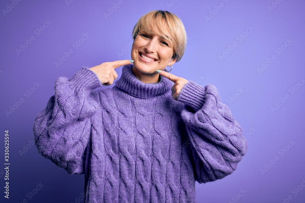 Young blonde woman with short hair wearing winter turtleneck sweater over purple background smiling cheerful showing and pointing with fingers teeth and mouth. Dental health concept. Young blonde woman with short hair wearing winter turtleneck sweater over purple background smiling cheerful showing and pointing with fingers teeth and mouth. Dental health concept.