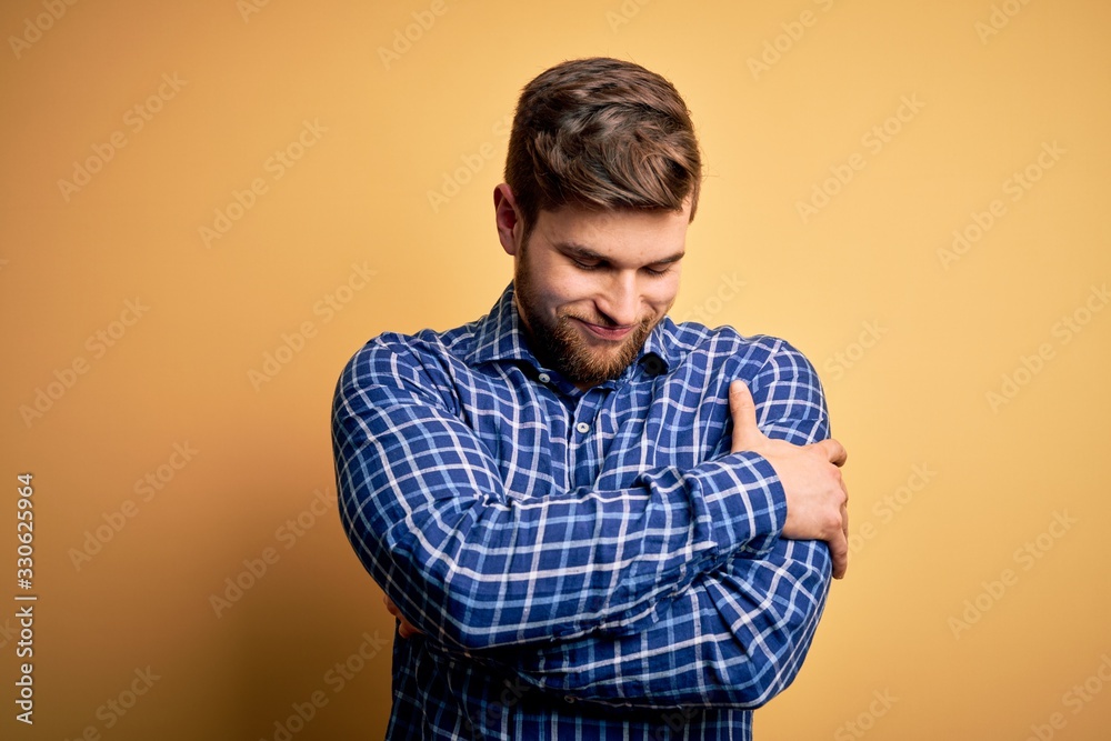 Young blond businessman with beard and blue eyes wearing shirt over yellow background Hugging oneself happy and positive, smiling confident. Self love and self care Young blond businessman with beard and blue eyes wearing shirt over yellow background Hugging oneself happy and positive, smiling confident. Self love and self care