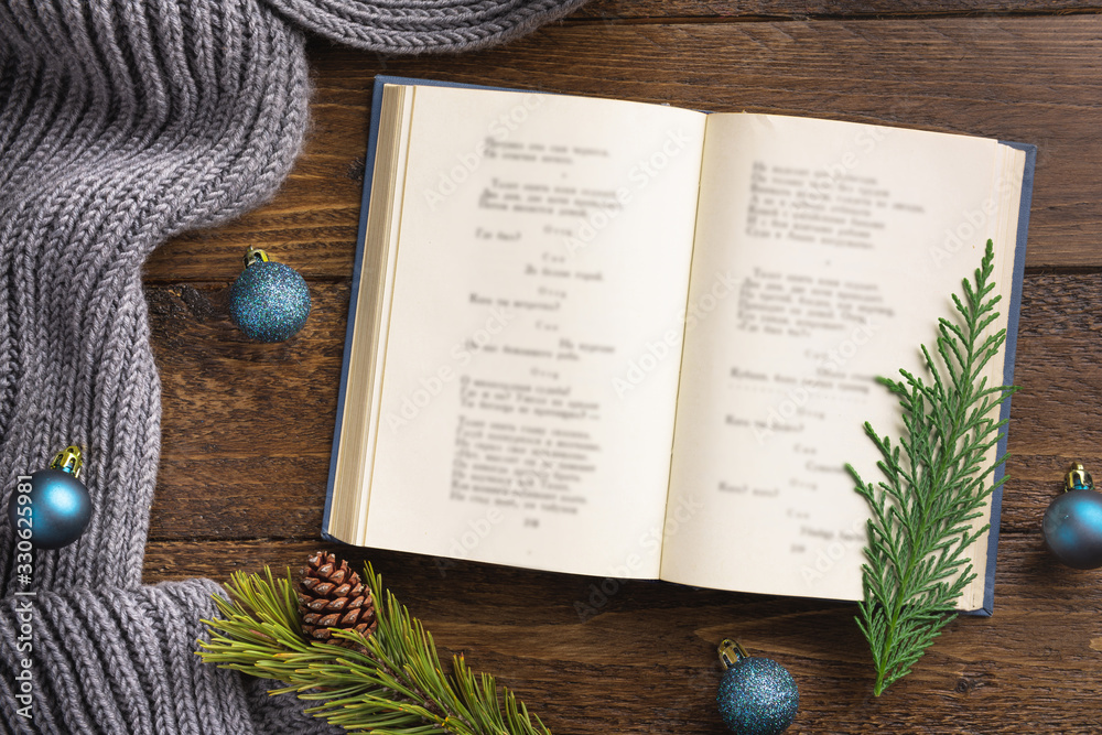 Fototapeta premium Flatlay composition with white knitted scarf, christmass decorations and open book on wooden desk table. Hygge style, cozy autumn or winter holiday concept. Flat lay, top view, overhead.