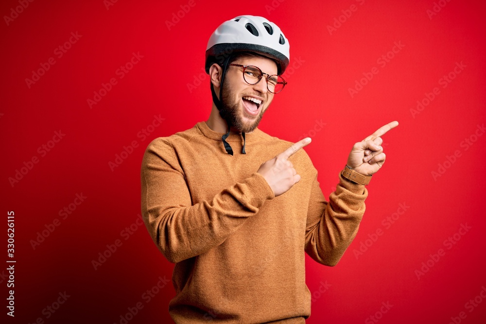 Young blond cyclist man with beard and blue eyes wearing bike helmet and glasses smiling and looking at the camera pointing with two hands and fingers to the side. Young blond cyclist man with beard and blue eyes wearing bike helmet and glasses smiling and looking at the camera pointing with two hands and fingers to the side.