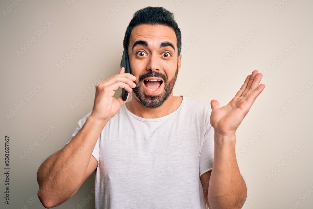 Young handsome man with beard having conversation talking on the smartphone very happy and excited, winner expression celebrating victory screaming with big smile and raised hands Young handsome man with beard having conversation talking on the smartphone very happy and excited, winner expression celebrating victory screaming with big smile and raised hands