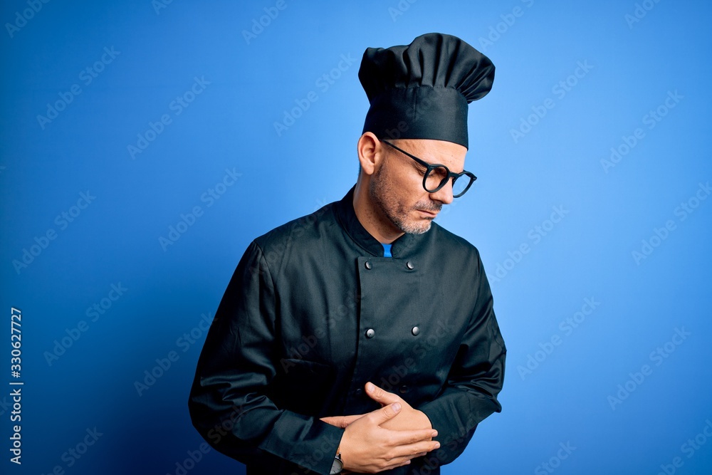 Young handsome chef man wearing cooker uniform and hat over isolated blue background with hand on stomach because indigestion, painful illness feeling unwell. Ache concept. Young handsome chef man wearing cooker uniform and hat over isolated blue background with hand on stomach because indigestion, painful illness feeling unwell. Ache concept.