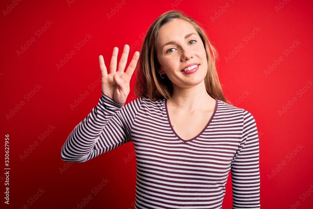 Young beautiful blonde woman wearing casual striped t-shirt over isolated red background showing and pointing up with fingers number four while smiling confident and happy. Young beautiful blonde woman wearing casual striped t-shirt over isolated red background showing and pointing up with fingers number four while smiling confident and happy.