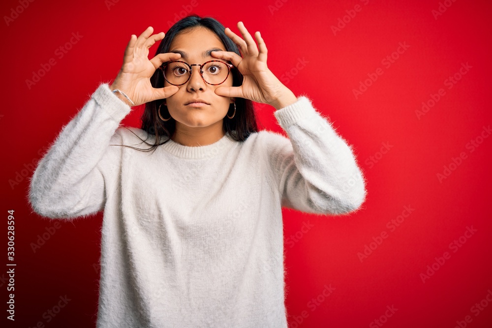 Young beautiful asian woman wearing casual sweater and glasses over red background Trying to open eyes with fingers, sleepy and tired for morning fatigue