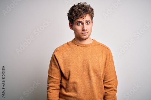 Young blond handsome man with curly hair wearing casual sweater over white background skeptic and nervous, frowning upset because of problem. Negative person.
