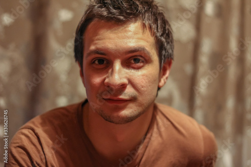 Portrait of a young seriously man at home on the background of the bookcase looking to camera.