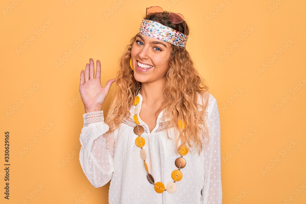 Young beautiful blonde hippie woman with blue eyes wearing sunglasses and accessories Waiving saying hello happy and smiling, friendly welcome gesture Young beautiful blonde hippie woman with blue eyes wearing sunglasses and accessories Waiving saying hello happy and smiling, friendly welcome gesture