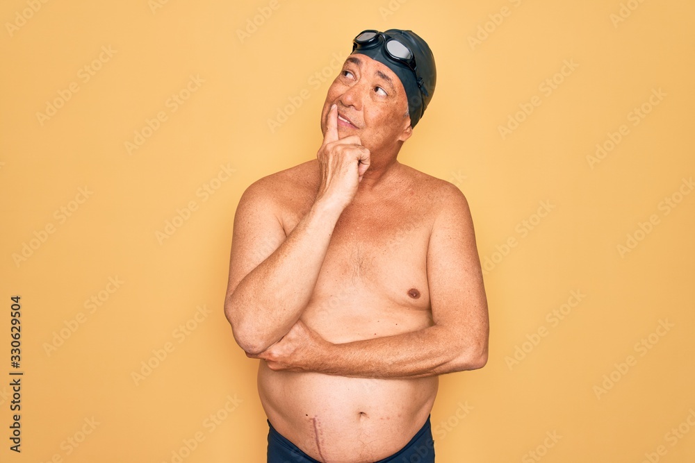 Middle age senior grey-haired swimmer man wearing swimsuit, cap and goggles Thinking worried about a question, concerned and nervous with hand on chin
